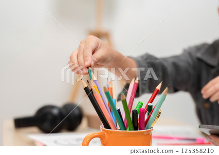 Art Supplies and Organization. A child selecting colored pencils from a container for drawing. 125358210