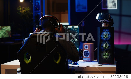 Man playing SF space videogame on PC screen in neon illuminated apartment living room. Gamer enjoying spaceship flying game on computer desktop display in RGB lit home late at night, camera A Man playing SF space videogame on PC screen in neon illuminated apartment living room. Gamer enjoying spaceship flying game on computer desktop display in RGB lit home late at night, camera A 125358428