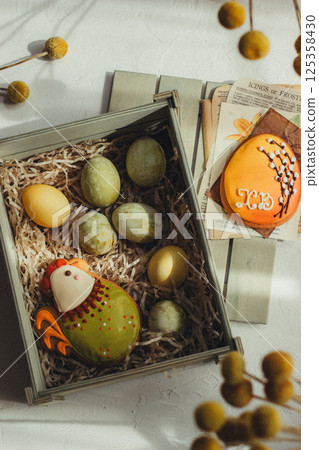 Close up of colorful Easter eggs in a wooden box, Easter cookies chicken and egg and decorations on the background, vintage style Close up of colorful Easter eggs in a wooden box, Easter cookies chicken and egg and decorations on the background, vintage style 125358430