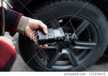 Close up of man hand holds a wireless portable air pump for inflating car tires. Self service, maintenance and safety.  125358472