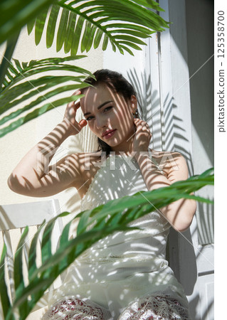Beautiful brunette woman in summer sitting in the shade of a palm tree Beautiful brunette woman in summer sitting in the shade of a palm tree 125358700