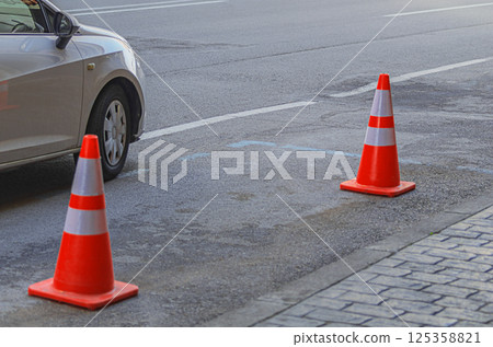 Empty parking place along on the side of a four-lane road with markings separating the directions of traffic, space for a car is reserved with orange and red plastic traffic cones 125358821