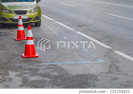 Empty parking place along on the side of a four-lane road with markings separating the directions of traffic, space for a car is reserved with orange and red plastic traffic cones 125358822