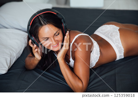 Brunette in lingerie listening to music in headphones and dancing in bedroom Brunette in lingerie listening to music in headphones and dancing in bedroom 125359018