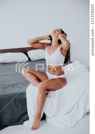 Brunette in lingerie listening to music in headphones and dancing in bedroom 125359020