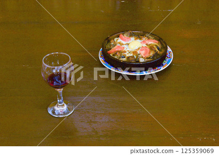 A glass of homemade georgian wine and the national Georgian dish is meat baked in the oven in a special cast-iron dish with vegetables and egg 125359069