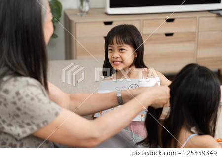 Family and Care. A grandmother lovingly styling her granddaughter's hair while she holds her artwork. 125359349