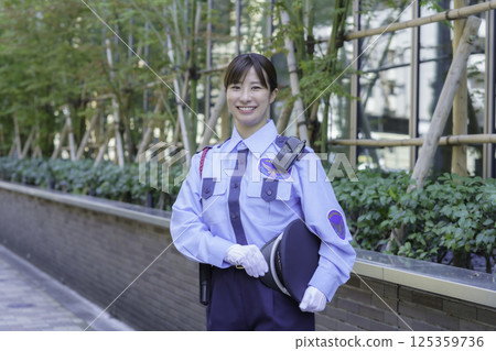A young female security guard standing in front of an office building. Photo courtesy of Tokyo Electronics College, Denpa Gakuen Corporation. 125359736