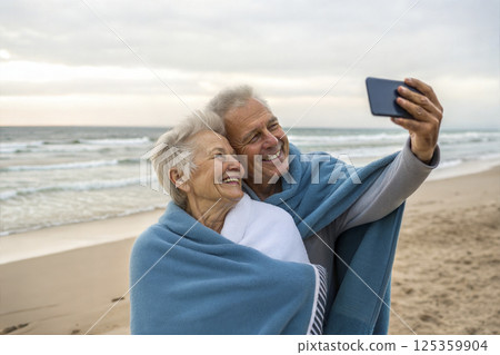 An elderly couple takes a selfie on the beach, wrapped in a towel, enjoying the golden years An elderly couple takes a selfie on the beach, wrapped in a towel, enjoying the golden years 125359904