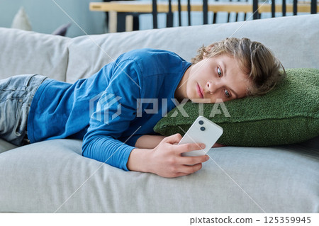 Serious teenager guy looking at smartphone screen lying on the couch at home 125359945
