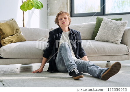 Portrait of handsome relaxed teenage boy sitting on floor near sofa in living room Portrait of handsome relaxed teenage boy sitting on floor near sofa in living room 125359953