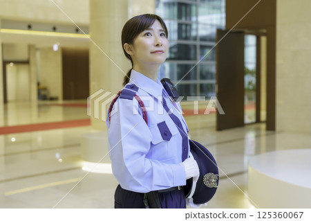 A young female security guard standing in the lobby of an office building. Photo courtesy of Tokyo Electronics College, Denpa Gakuen Corporation. 125360067