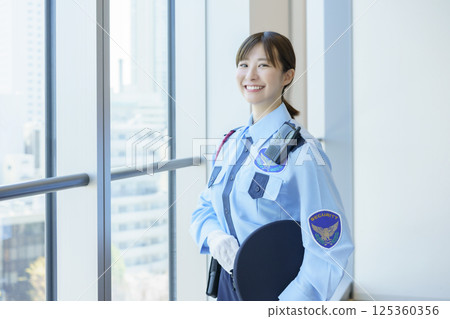 Portrait of a young female security guard standing by a window. Photo courtesy of Tokyo Electronics College, Denpa Gakuen School Corporation. 125360356