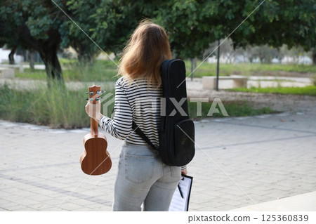 Girl Walks With Ukulele And Backpack Musical Instrument In City Park Girl Walks With Ukulele And Backpack Musical Instrument In City Park 125360839