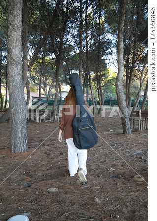 Girl Walks With Guitar Bass Instrument Case Behind Her In The Park Girl Walks With Guitar Bass Instrument Case Behind Her In The Park 125360846