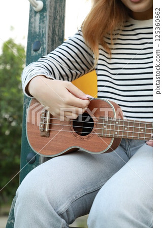 Girl Artist Hands Practices Playing The Ukulele In A Green Meadow Girl Artist Hands Practices Playing The Ukulele In A Green Meadow 125360862