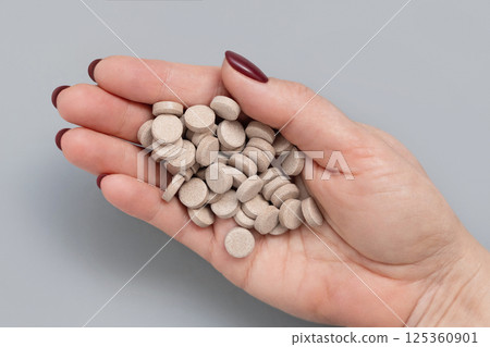 Cupped womans hand with a pile of beige medical pills top view over grey Cupped womans hand with a pile of beige medical pills top view over grey 125360901