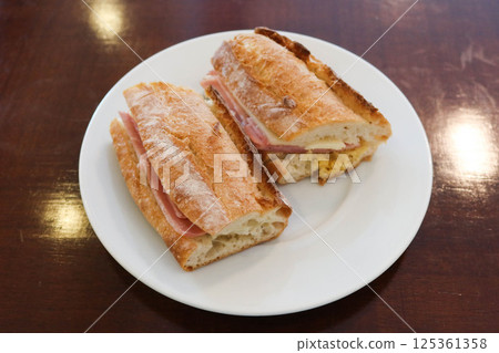 close up of a Baguette bread sandwich with ham and cheese cut in two half on a white plate with copy space close up of a Baguette bread sandwich with ham and cheese cut in two half on a white plate with copy space 125361358