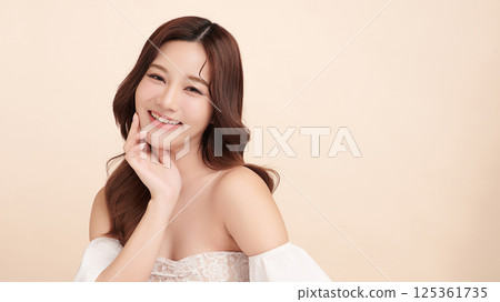 A beautiful young Asian woman with clean, fresh skin against a beige background. Skincare, facial treatment, cosmetology, beauty, and spa. An elegant portrait of an Asian woman. A beautiful young Asian woman with clean, fresh skin against a beige background. Skincare, facial treatment, cosmetology, beauty, and spa. An elegant portrait of an Asian woman. 125361735