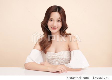 A beautiful young Asian woman with clean, fresh skin against a beige background. Skincare, facial treatment, cosmetology, beauty, and spa. An elegant portrait of an Asian woman. 125361740