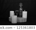 three burning candles on the oak stand with a glass and a bottle of homemade strong drink  125361803