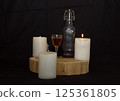 three burning candles on the oak stand with a glass and a bottle of homemade strong drink  125361805
