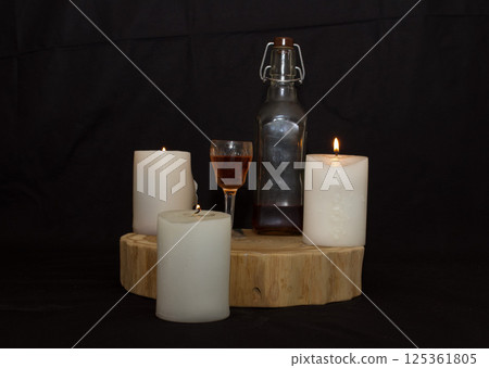 three burning candles on the oak stand with a glass and a bottle of homemade strong drink three burning candles on the oak stand with a glass and a bottle of homemade strong drink 125361805