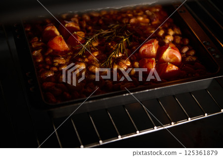 A baking dish filled with beans, tomatoes, and herbs is baking in an oven under warm light. The rustic preparation creates an inviting atmosphere, highlighting the freshness and simple cuisine. A baking dish filled with beans, tomatoes, and herbs is baking in an oven under warm light. The rustic preparation creates an inviting atmosphere, highlighting the freshness and simple cuisine. 125361879