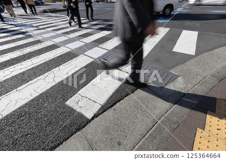 An intersection with a crosswalk. A businessman crossing the crosswalk on his way to work in the morning. 125364664
