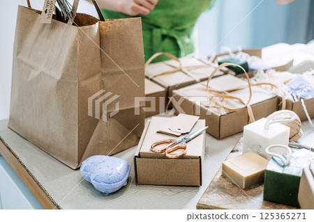 A collection of natural handmade soap bars, cardboard packaging, and eco-friendly gift wrapping tools on a tabletop. Sustainability, small business support, artisan craftsmanship, zero waste packaging 125365271