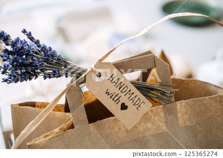 Close-up of a brown paper bag with a handwritten tag reading Handmade with love and a sprig of lavender. Handmade with love, emotional branding, artisan identity, heartfelt storytelling 125365274