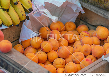 A wooden box with orange ripe apricots and bananas for sale in the city market - fair. Fruit stall, farm products. Natural healthy food for humans, saturated with vitamins and trace elements A wooden box with orange ripe apricots and bananas for sale in the city market - fair. Fruit stall, farm products. Natural healthy food for humans, saturated with vitamins and trace elements 125365582