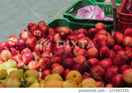 Red and yellow striped natural ripe fruit juicy delicious peaches and golden, green apples stacked on top of each other in a stall in the market on the background of fruit plastic boxes 125365585