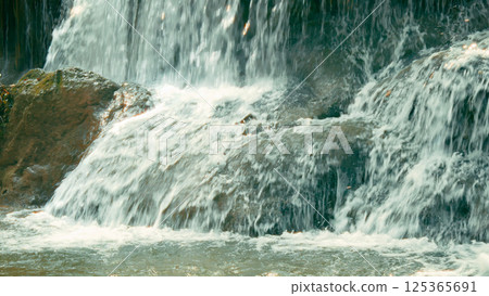Close-up of cascading waterfall flowing over rugged rocks, capturing the dynamic movement of water in natural forest 125365691
