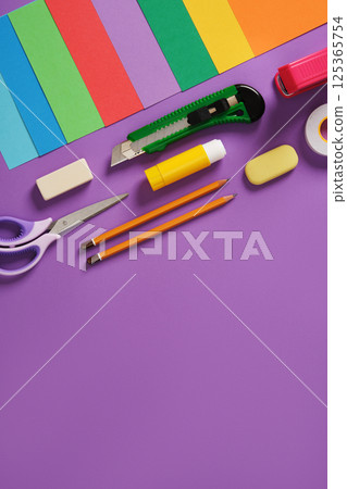 Paper craft table: scissors, knife, pencil, eraser, colored paper on purple background. Space for your text. Paper craft table: scissors, knife, pencil, eraser, colored paper on purple background. Space for your text. 125365754