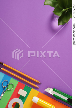 Paper craft table: scissors, knife, pencil, eraser, colored paper on purple background. Space for your text. Paper craft table: scissors, knife, pencil, eraser, colored paper on purple background. Space for your text. 125365755