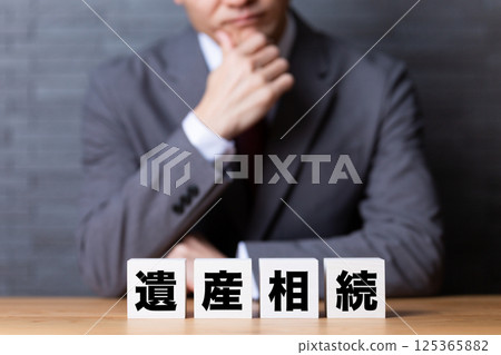 A middle-aged male businessman wearing a suit and worried about inheritance blocks 125365882