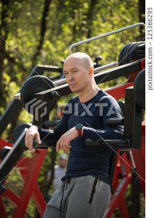 Muscular sportsman resting after training outdoors wearing black t-shirt at outdoor open training park gym. Outdoors. Healthy lifestyle. 125366295