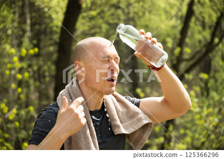 Sporty man refreshing himself water from bottle against forest at summer heat after training outdoors. Hiking. Concept water balance. Close up. 125366296