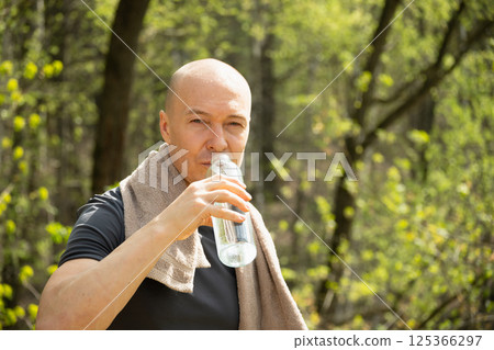 Sporty man drinking water from bottle against forest at summer heat after training outdoors. Hiking. Concept water balance. Close up. 125366297