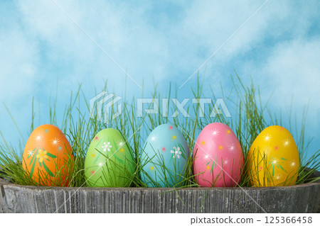 Colorful Easter eggs in flower pot with grass on blue sky background. Copy space 125366458