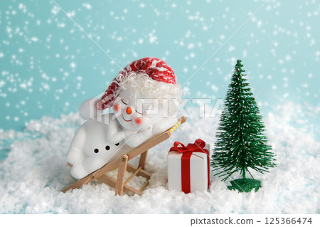 Snowman is relaxing on sun lounger. christmas eve noel. time to relax. Snowman, Christmas Tree and gift box on blue background. Winter holiday concept Snowman is relaxing on sun lounger. christmas eve noel. time to relax. Snowman, Christmas Tree and gift box on blue background. Winter holiday concept 125366474