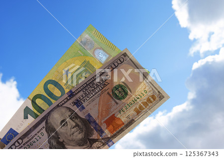 One hundred euros and one hundred dollars against a sky with clouds. The money is transparent. It's your choice. One hundred euros and one hundred dollars against a sky with clouds. The money is transparent. It's your choice. 125367343