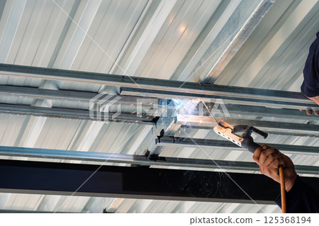 Metalworker welding steel frame of roof structure in industrial workshop 125368194