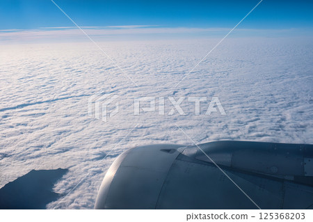Airplane window with aircraft engine above white clouds with sky view Airplane window with aircraft engine above white clouds with sky view 125368203