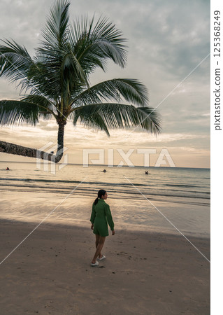 Asian woman walk along the beach under palm tree in the evening during summer vacation 125368249