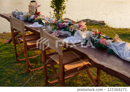 Romantic elegant dining setup with wooden long table, chairs, tableware, cutlery, candle and flora decoration 125368271