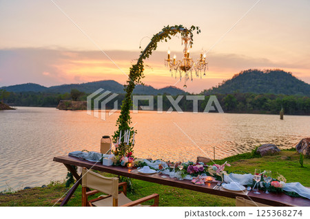 Romantic elegant dining setup with wooden long table, chairs, tableware, cutlery, candle and flora decoration 125368274
