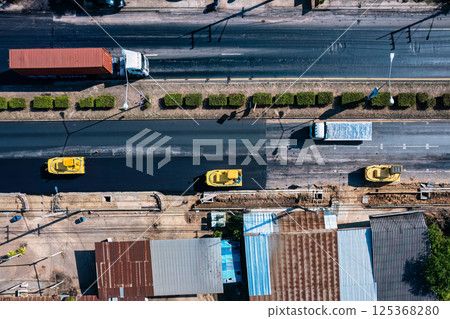 Top view of yellow construction vehicle working with paving on urban road in improvement project Top view of yellow construction vehicle working with paving on urban road in improvement project 125368280