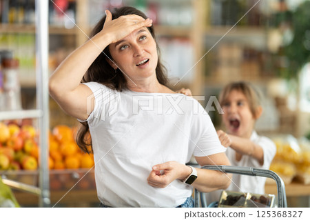 Tired and angry mother with basket of groceries in her hands quarreling with her little daughter. 125368327